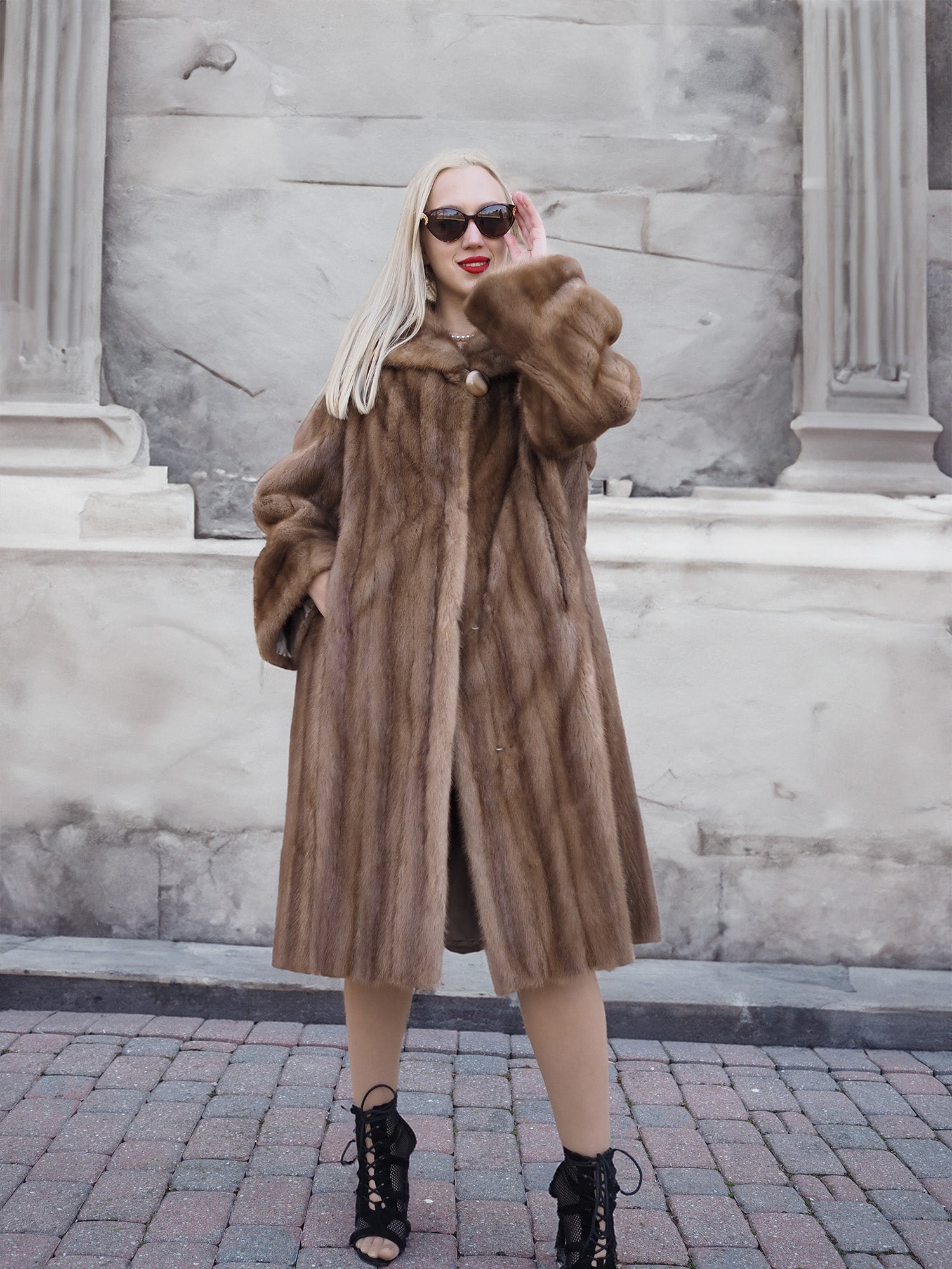 Stylish pastel brown mink fur coat on model against stone building