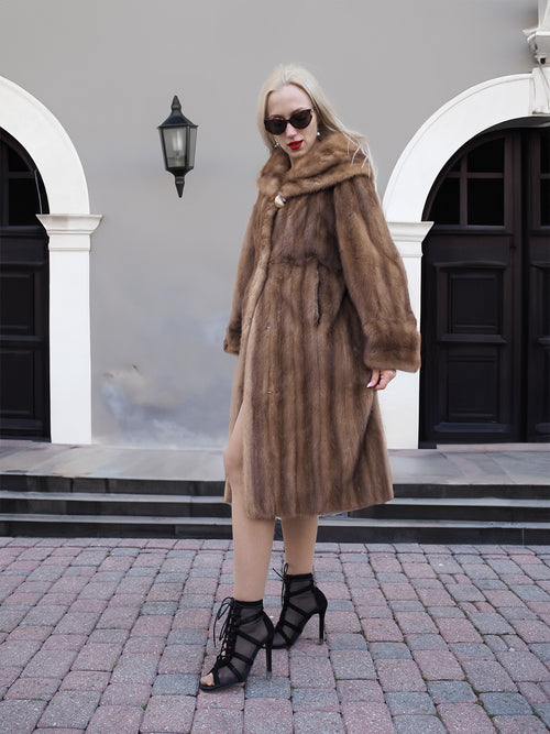 Luxurious pastel brown mink fur coat in classic stroller style, worn by a fashionable woman outside an elegant building.
