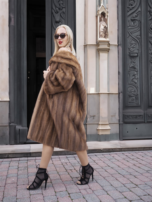 Luxurious vintage Canadian brown mink fur coat with stroller-length design, worn by fashionable woman in front of ornate architecture.