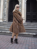 Elegant vintage pastel brown mink fur coat, luxurious full-length stroller style, worn by fashionable woman outside architectural building.