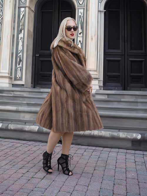Elegant vintage pastel brown mink fur coat, luxurious full-length stroller style, worn by fashionable woman outside architectural building.
