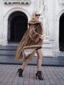 Luxurious pastel brown mink fur coat on stylish model, showcasing high-end fashion accessories in front of ornate architectural backdrop.