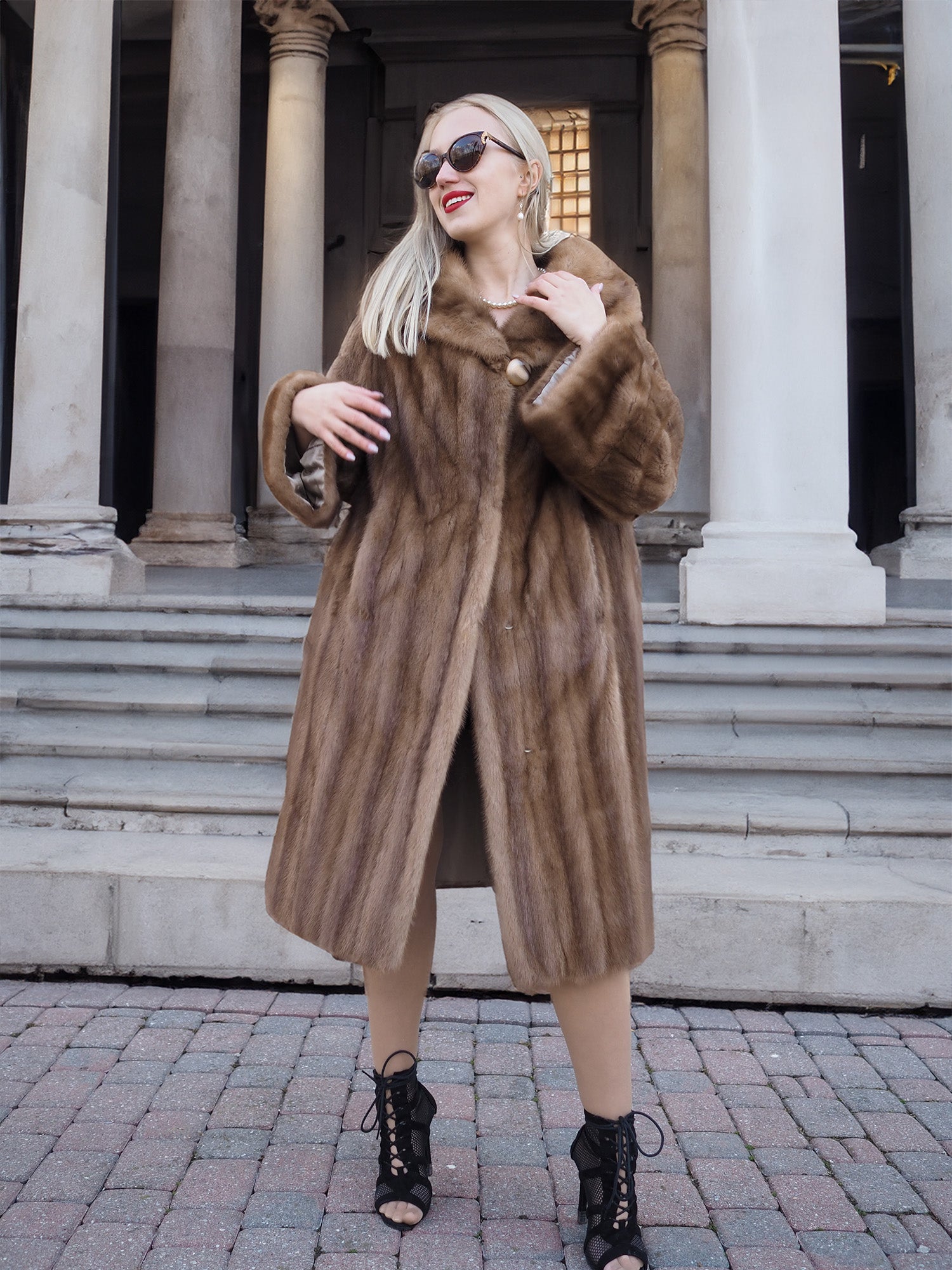 Elegant pastel brown mink fur coat with flowing silhouette, worn by a stylish woman in front of a historic building.