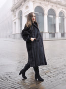 Model in black mink fur coat walking on cobblestone street, showcasing timeless elegance in luxury outerwear.