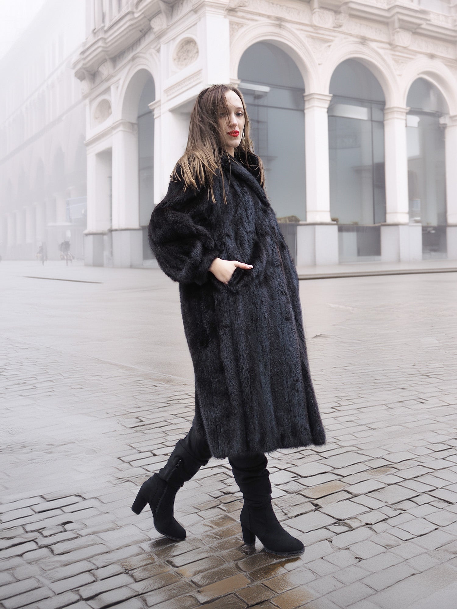 Model in black mink fur coat walking on cobblestone street, showcasing timeless elegance in luxury outerwear.