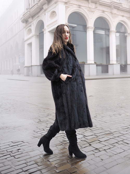 Model in black mink fur coat walking on cobblestone street, showcasing timeless elegance in luxury outerwear.