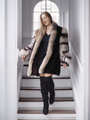 Woman in a fur coat and black boots walking down a staircase.