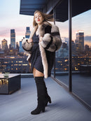 Woman in a fur coat and black dress standing on a balcony with city skyline view