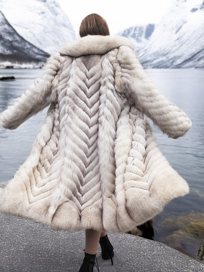 Chic blue fox fur coat with large collar in snowy landscape.