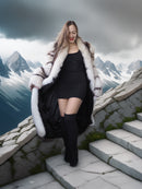 Woman in a fur coat standing on stone steps with mountains in the background