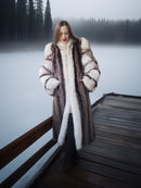 Woman in a fur coat standing on a dock by a lake with trees in the background