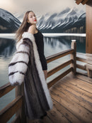 Woman in a fur coat standing on a wooden deck with a mountain and lake background