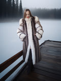 Woman in a fur coat standing on a dock by a lake with trees in the background