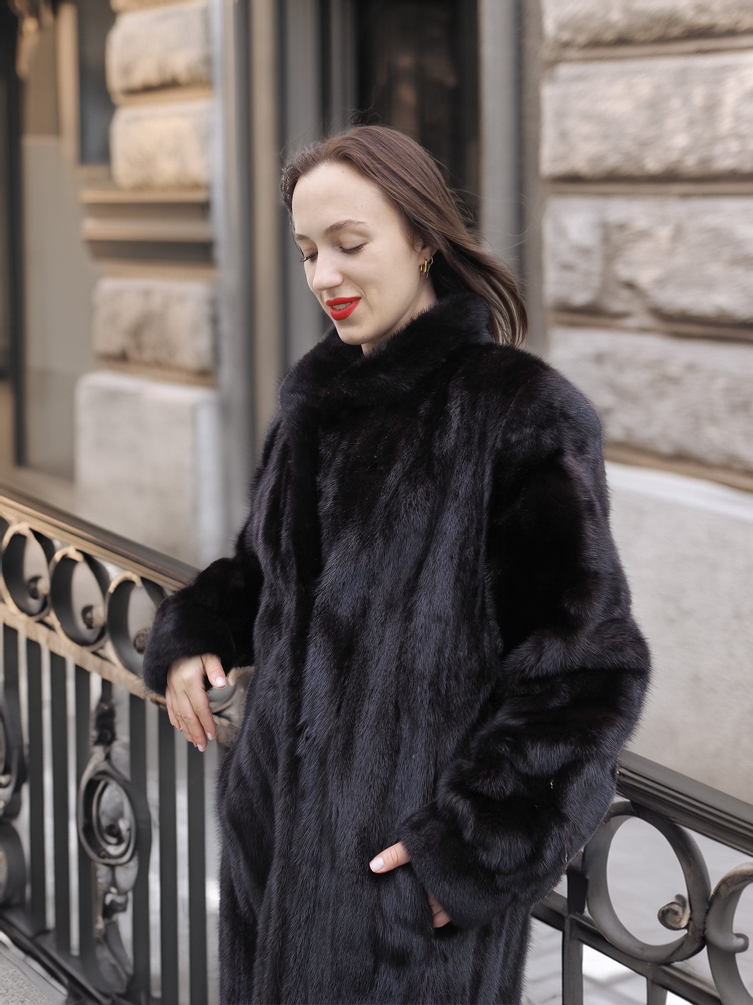 Woman leaning on railing in Midnight Sonata black mink coat, highlighting the coat’s plush texture and timeless sophistication.