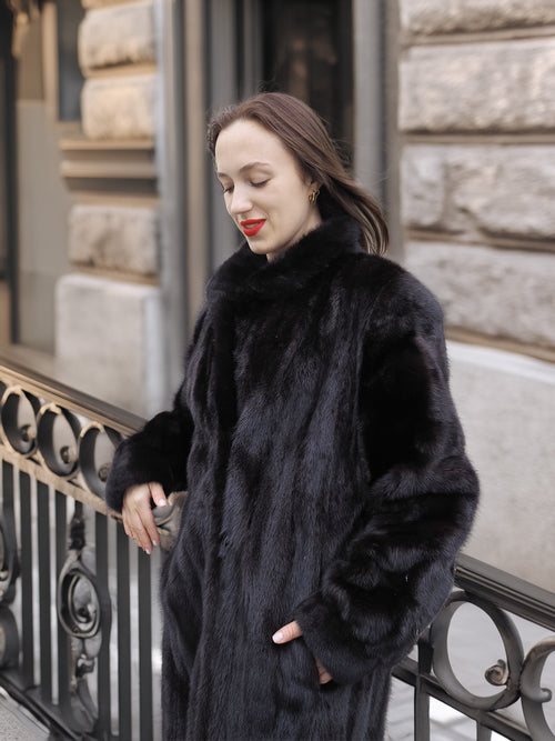 Woman leaning on railing in Midnight Sonata black mink coat, highlighting the coat’s plush texture and timeless sophistication.