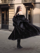 Woman twirling in Midnight Sonata black mink coat, highlighting the coat's dramatic motion and luxurious fur texture in an urban setting.