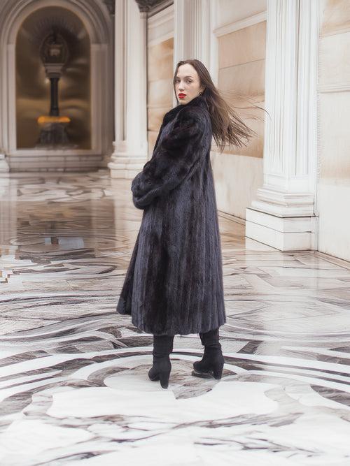 Model turning in Midnight Sonata black mink coat, showcasing its elegant drape and premium fur quality in a palace setting.