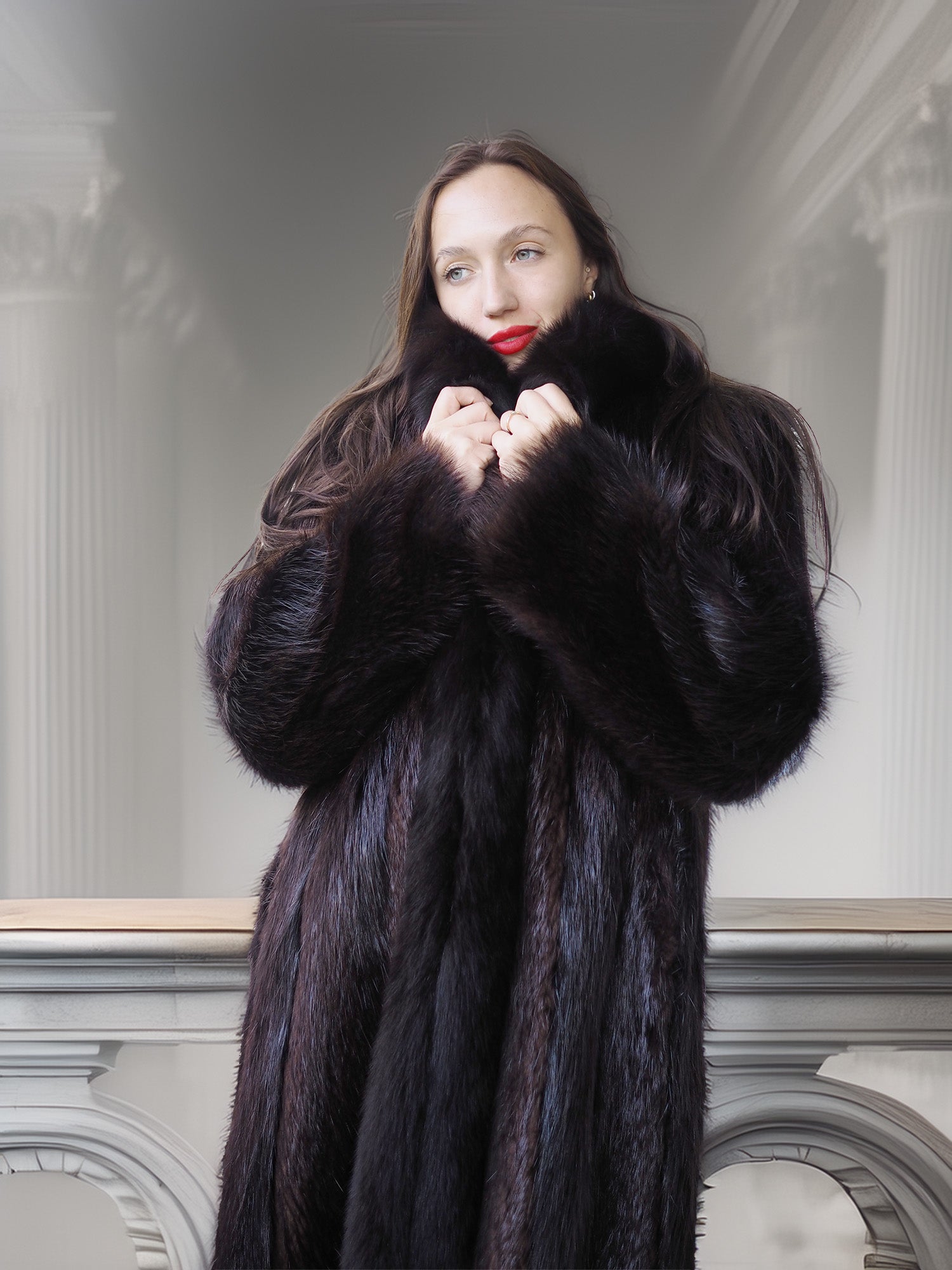 Woman wearing a long black fur coat in an elegant interior setting.