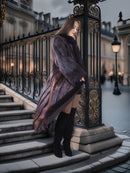 Woman in a fur coat standing behind an ornate black gate in an urban setting