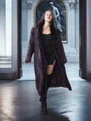 Woman in a long dark coat standing in an elegant hallway with classical architecture.