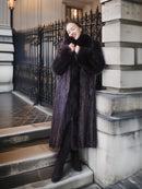 Woman in a fur coat standing on steps with a decorative metal railing in the background