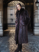 Woman in a fur coat standing in an elegant outdoor setting with architectural elements.