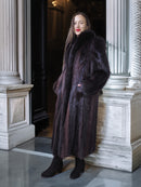Woman wearing a long dark fur coat standing in an elegant interior setting.