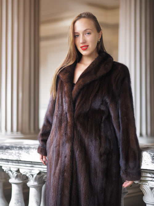 Woman wearing a dark brown fur coat standing in front of classical architecture.