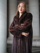 Woman wearing a brown fur coat standing in an indoor setting with columns.
