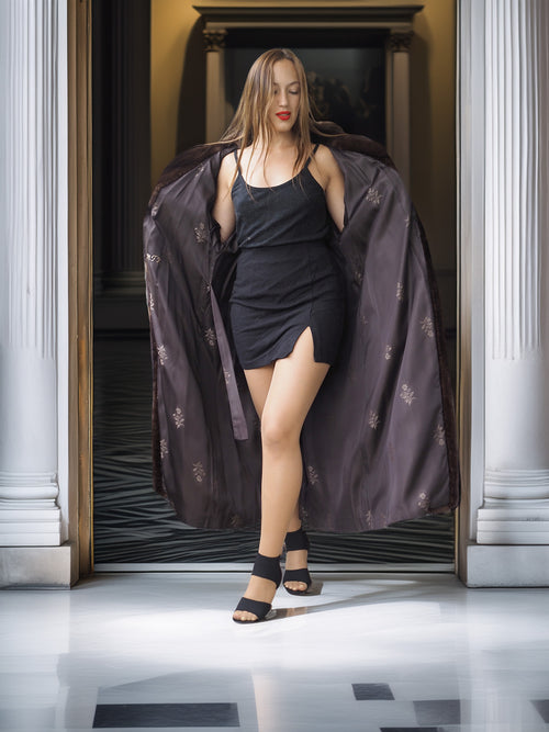 Woman in a black dress with a long, dark coat standing in a doorway.