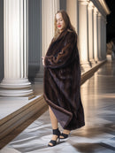 Woman in a long brown fur coat standing in front of classical columns.