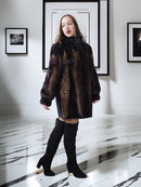 Woman wearing a dark patterned coat and black knee-high boots in an art gallery setting.