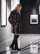 Woman in a fur coat and black boots standing in a modern interior setting.