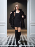 Woman in a black coat and dress with knee-high boots standing in a doorway.