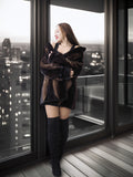 Woman in a fur coat and knee-high boots standing by a large window with a cityscape view.