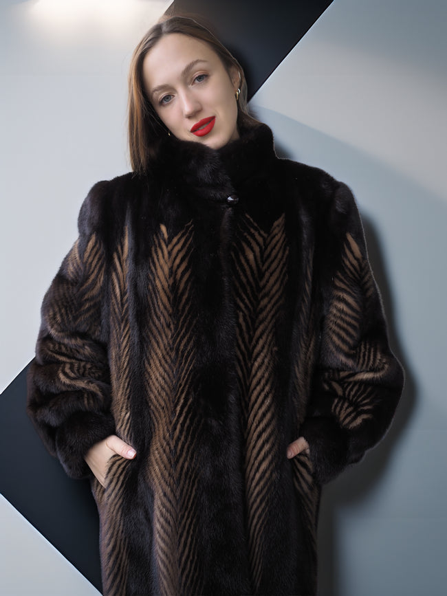 Woman wearing a dark fur coat with a geometric pattern against a plain background