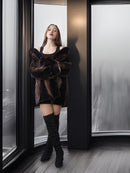 Woman in a black outfit with a fur coat standing in front of a glass door.