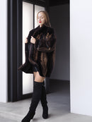 Woman wearing a dark fur coat and black knee-high boots in a minimalistic setting.
