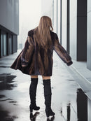 Person wearing a patterned coat and knee-high boots walking on a wet pavement.