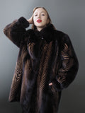 Woman wearing a dark fur coat with a patterned design against a gray background