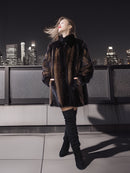 Woman in a patterned coat and knee-high boots standing on a rooftop with a city skyline in the background.