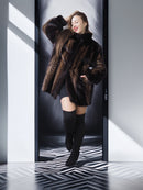 Woman in a fur coat and knee-high boots standing in a modern, minimalistic room with geometric floor.