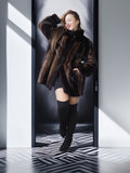 Woman in a fur coat and knee-high boots standing in a modern, minimalistic room with geometric floor.