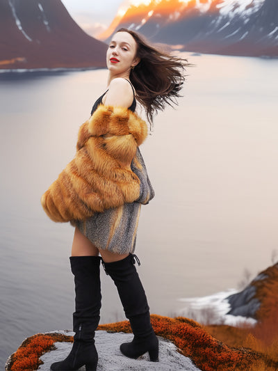 Luxury red and gray fox fur coat from The Wild Muse, showcased on a cliffside at sunset, highlighting its rich texture and cinematic elegance.