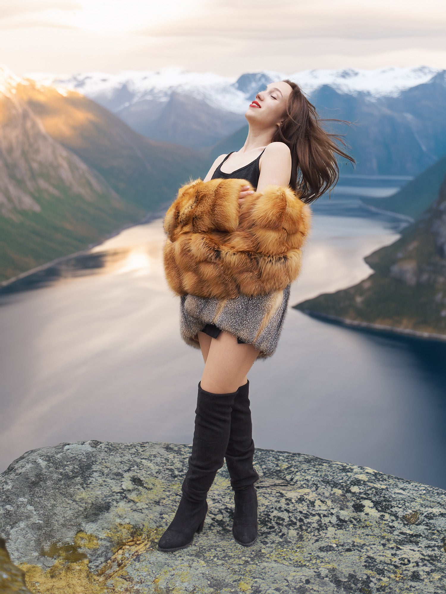The Wild Muse luxury fur coat in red and gray fox, styled with joy and movement atop a scenic cliff for a bold fashion statement.