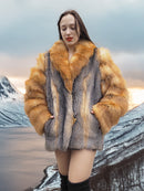 Red gray fox fur coat by The Wild Muse, styled with hands in pockets against a snowy mountain backdrop for a luxury winter look.