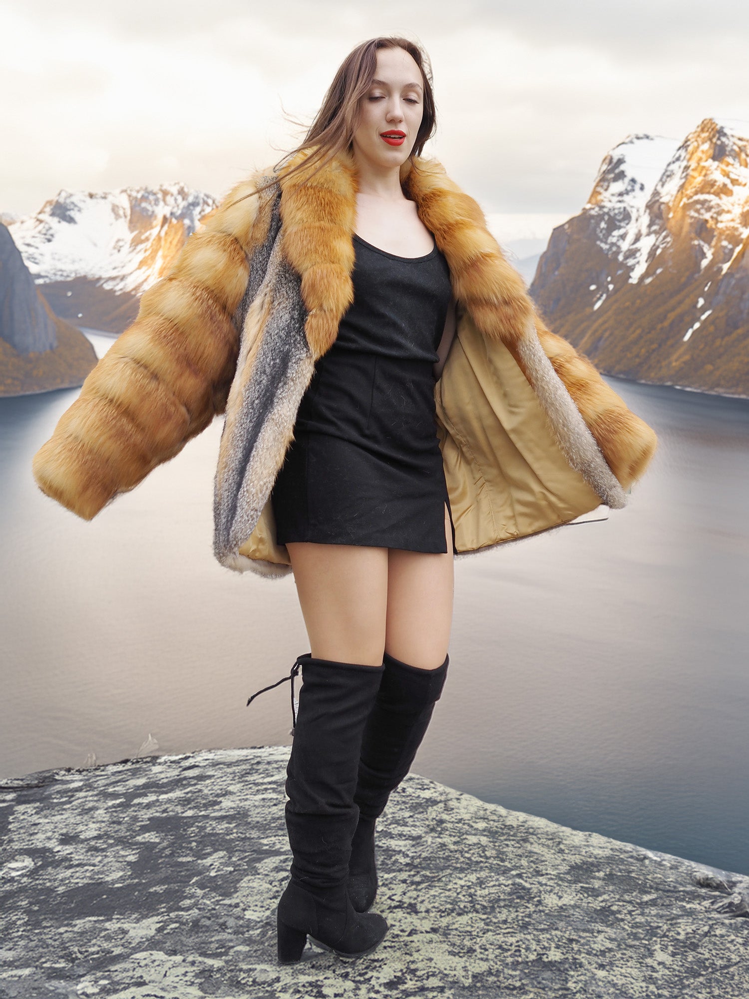 The Wild Muse fox fur coat in red and gray tones, opened to reveal golden lining, styled on a cliff with dramatic fjord views.