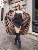 Model reveals the silky interior of the Harlow pastel mink coat, pairing it with a black dress and thigh-high boots.