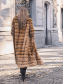 Back view of Harlow pastel mink coat with shawl collar, walking down a sunlit cobblestone street in vintage elegance.