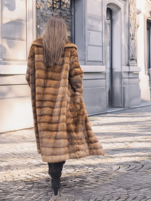 Back view of Harlow pastel mink coat with shawl collar, walking down a sunlit cobblestone street in vintage elegance.